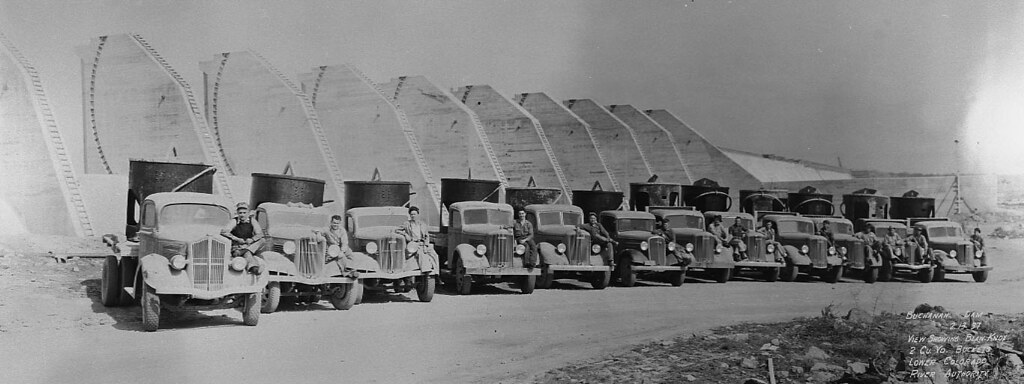 Drivers sit on the bumpers of their trucks loaded with cement funnels during the construction of Buchanan Dam, February 13, 1937.